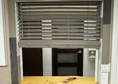 A wooden window frame with horizontal blinds featuring a mix of gray, white, and natural wood accents above a rustic wooden ledge.