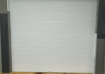 A white honeycomb shade covers a window, framed with rustic wooden panels in various shades, complemented by a natural wooden ledge.