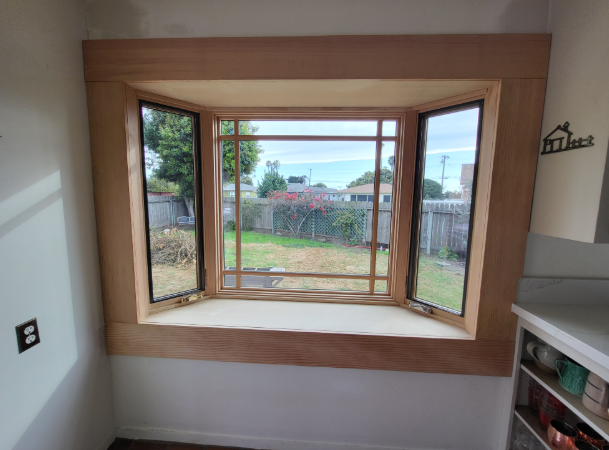Newly installed wooden bay window with side casement windows overlooking a backyard, showcasing professional residential window installation and natural wood interior finish.